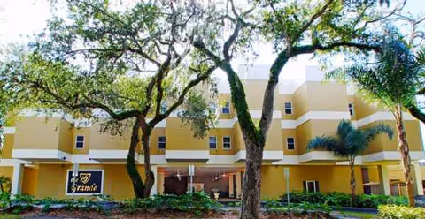 Yellow multi-story senior living building named The Grande with trees in front