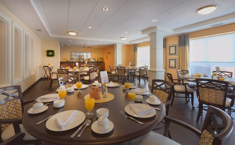 Bright dining room with round tables set for breakfast, chairs, and glasses of orange juice.