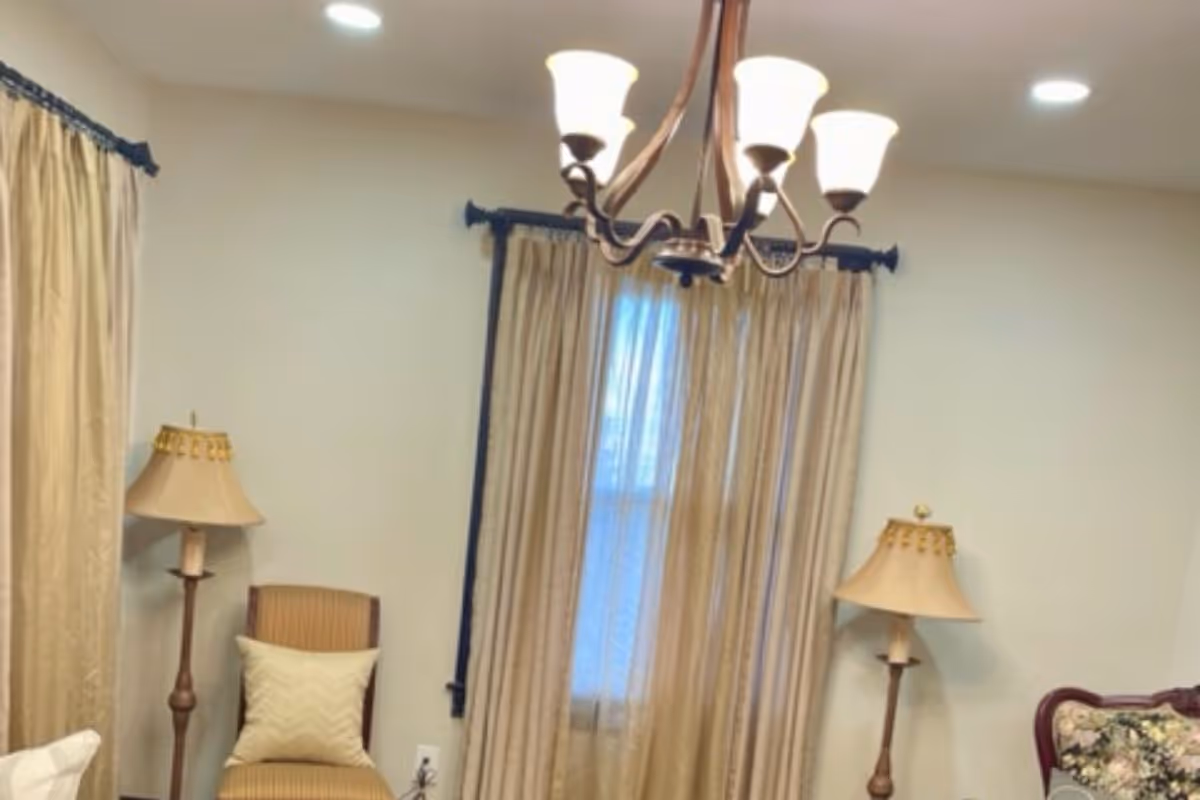 Living room scene with beige curtains, chandelier, and lamps in a calm senior living space.