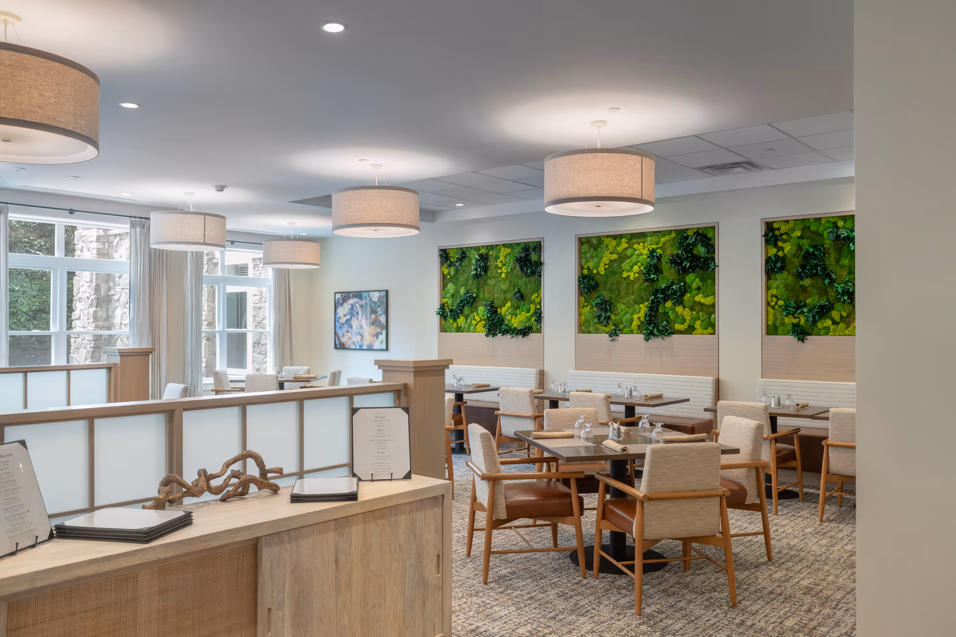 Bright dining room with tables and upholstered chairs, pendant lights, and green living-wall panels.