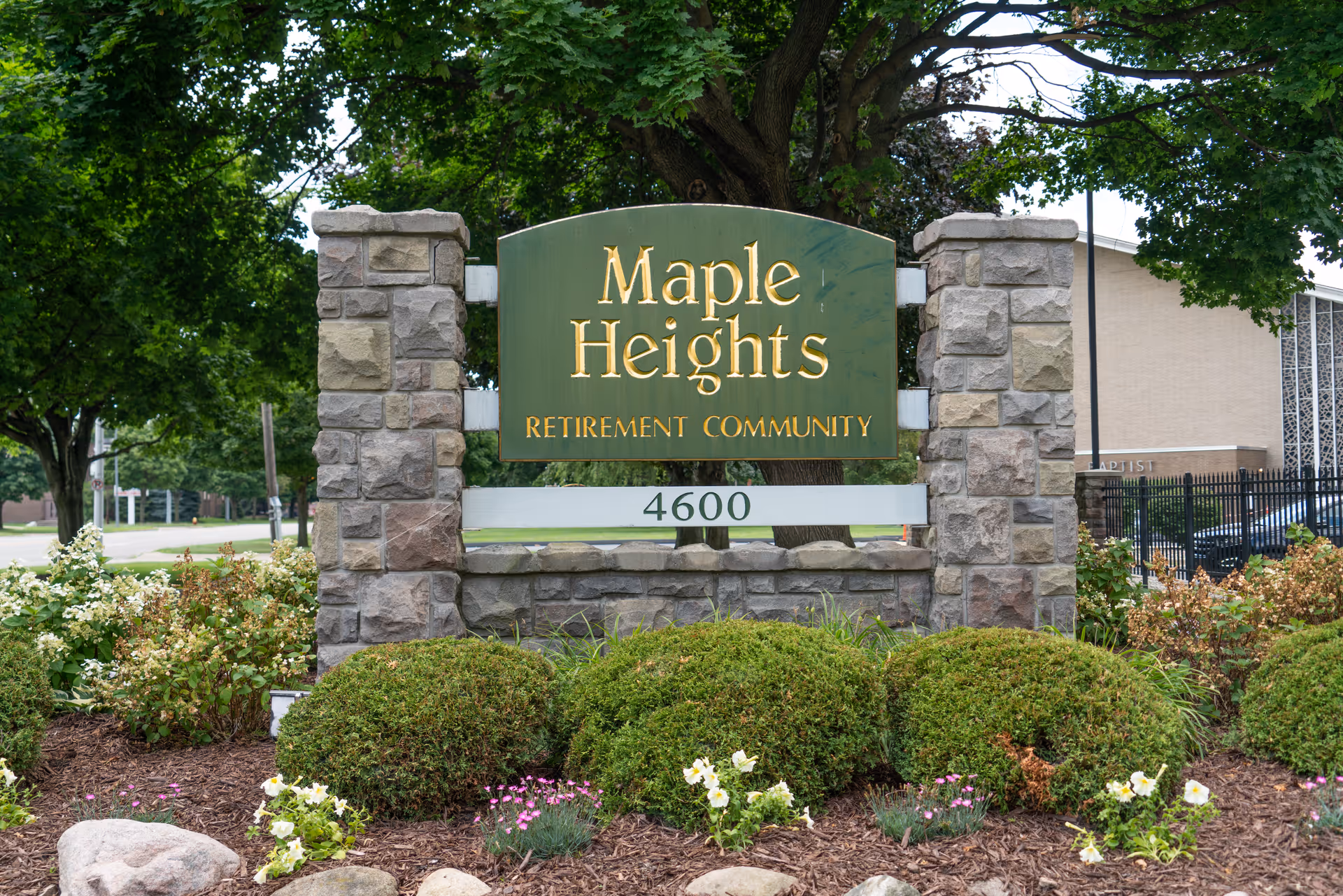 Stone entrance sign reading 'Maple Heights Retirement Community' with the address 4600, surrounded by shrubs and trees.