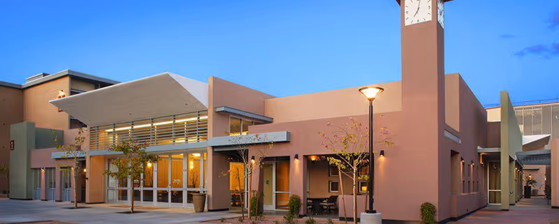 Beatitudes Campus building exterior with clock tower and glass entrance at dusk.