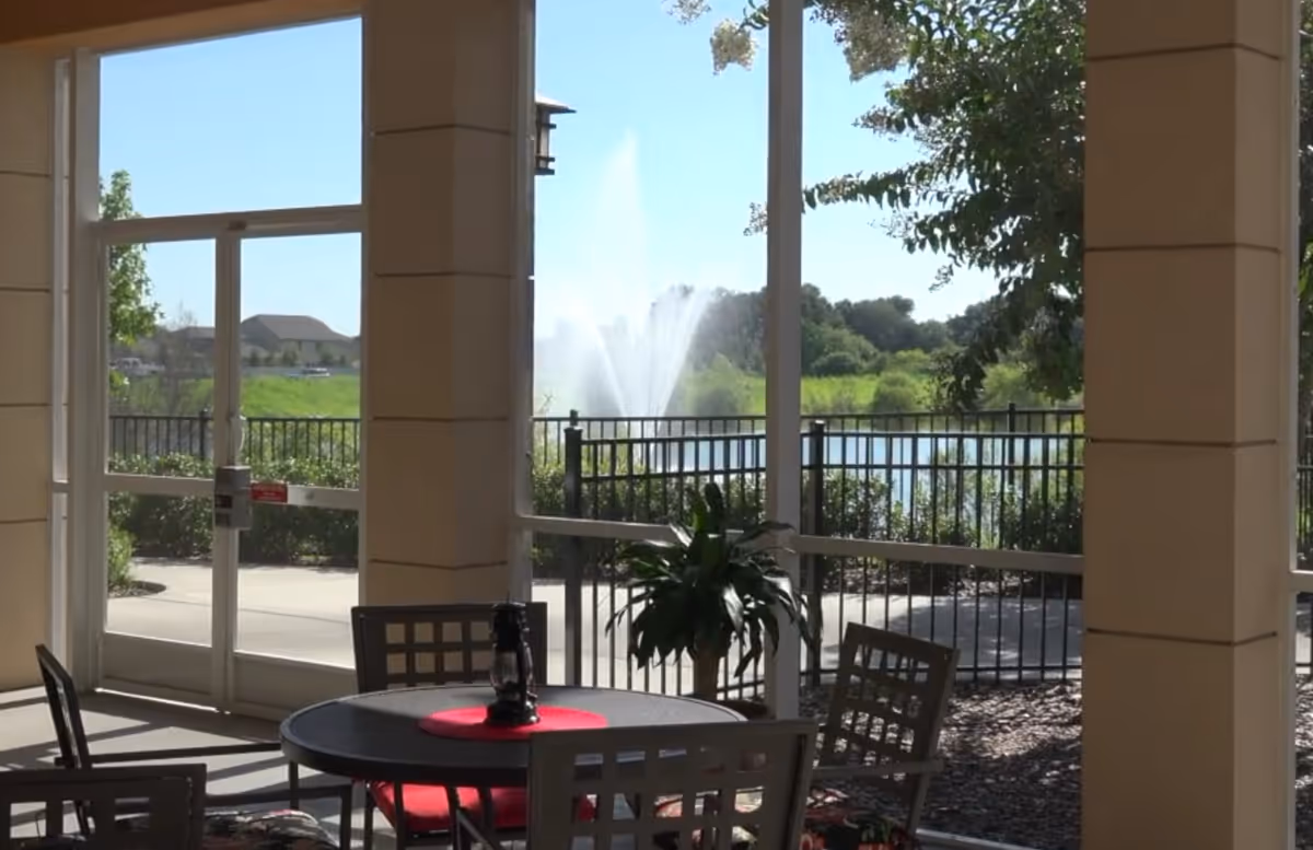 Indoor seating area with a round table and chairs by large windows looking out onto a pond with a fountain.