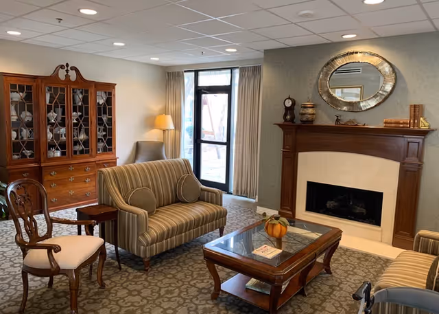 Comfortable living room with a striped loveseat and chairs around a wooden coffee table in front of a fireplace and china cabinet.