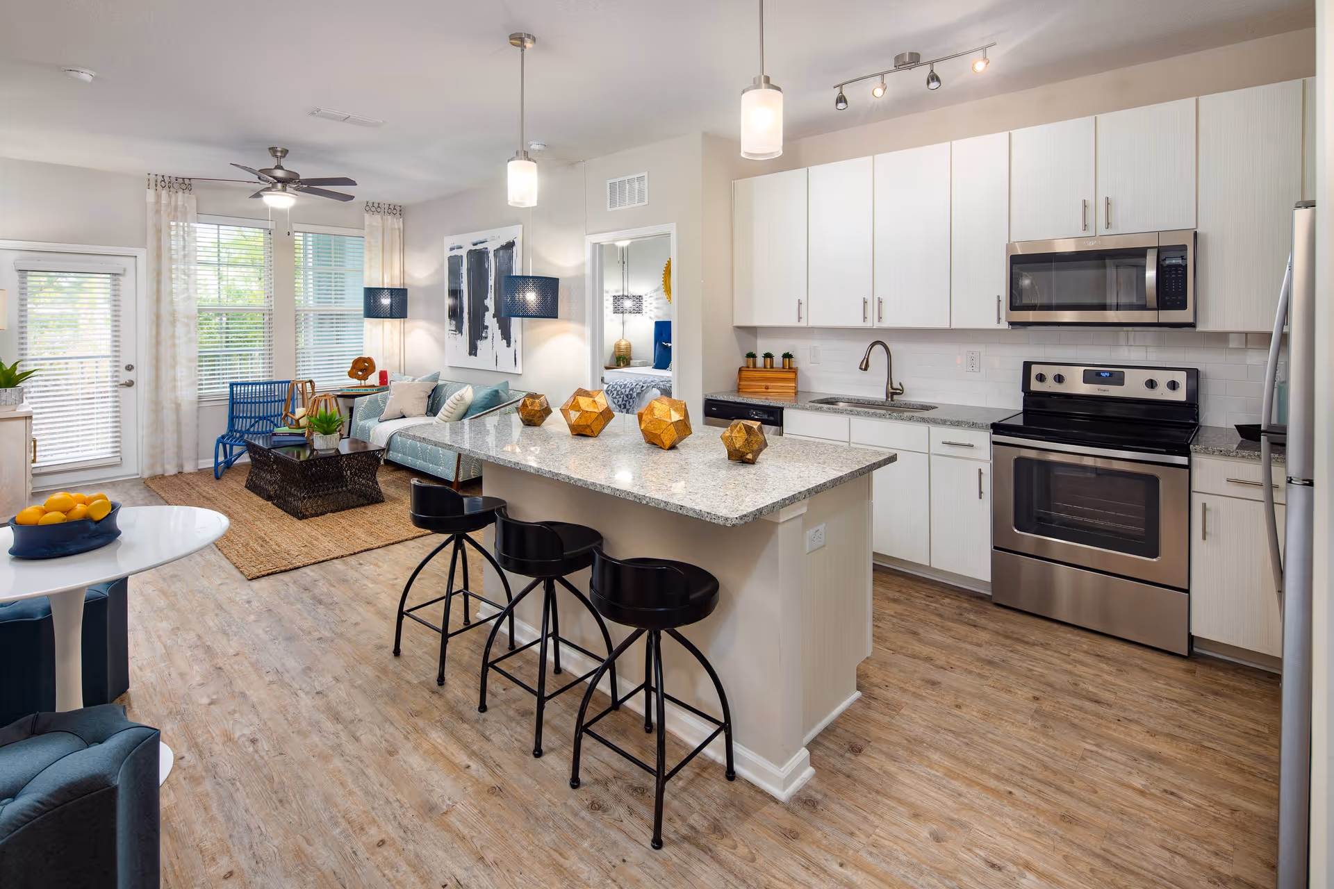 Open-plan living area and kitchen featuring a granite island with three bar stools, stainless steel appliances, and a sitting area.