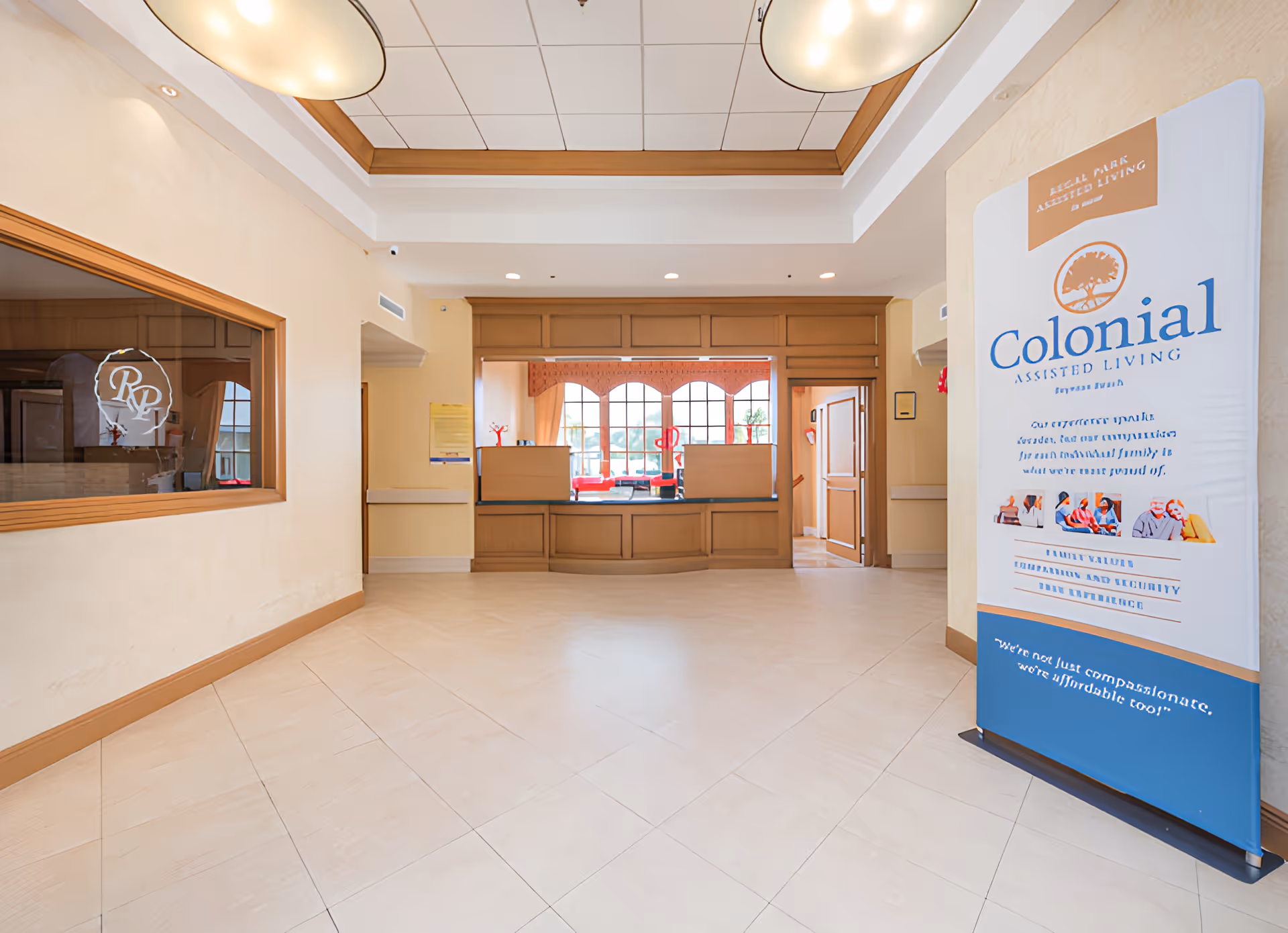 Lobby reception area with a front desk, windows, and a freestanding 'Colonial Assisted Living' banner.