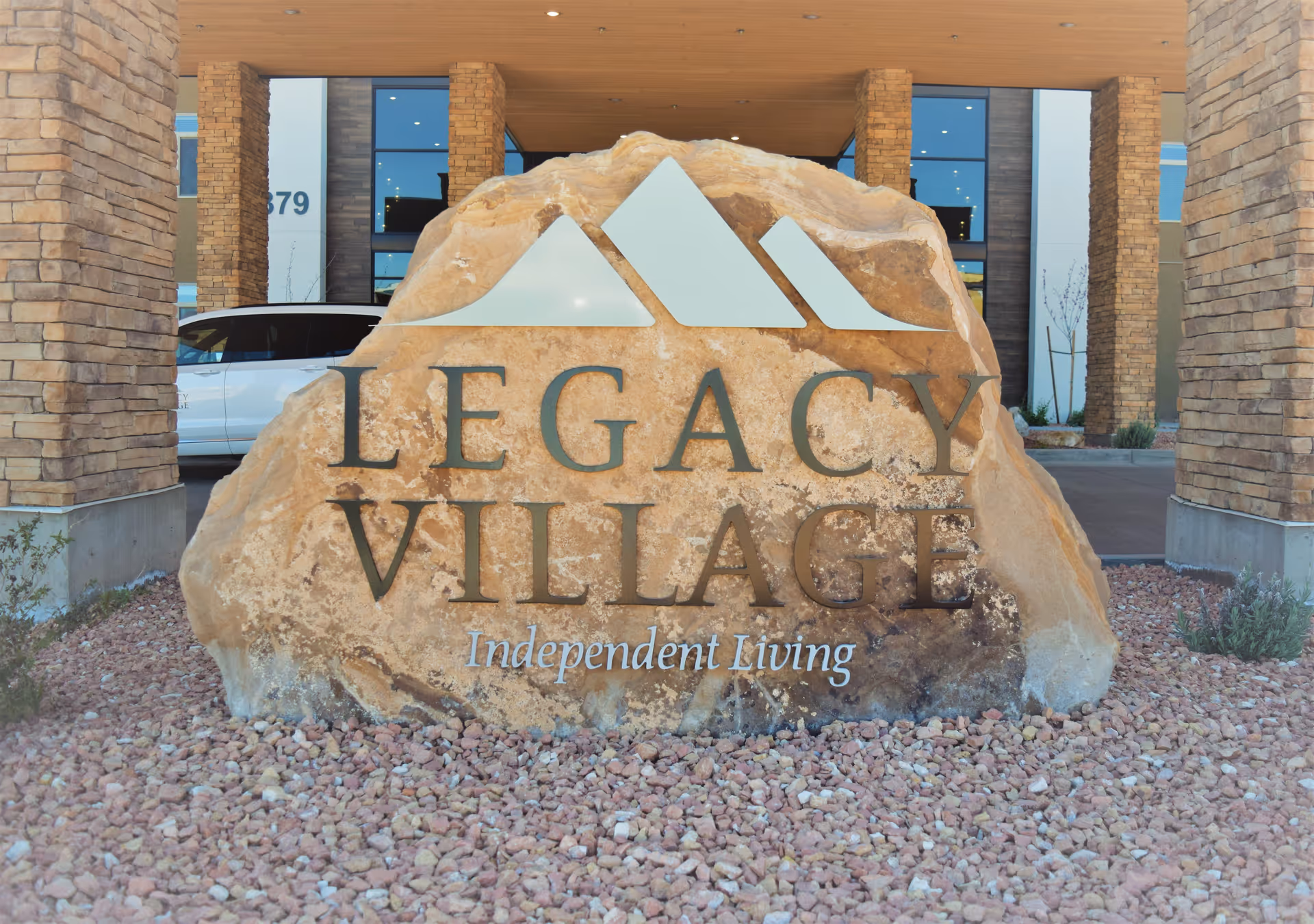 Large carved rock sign that reads "Legacy Village Independent Living" at the entrance of the facility.