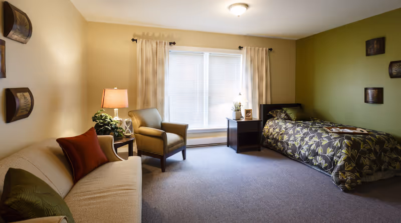 Sunny studio-style bedroom with a single bed, sofa, armchair, side tables, and a large window.