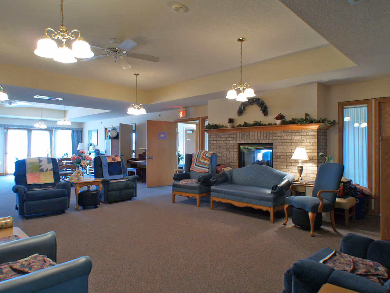 Spacious communal living room with sofas and armchairs arranged around a brick fireplace and overhead lighting.