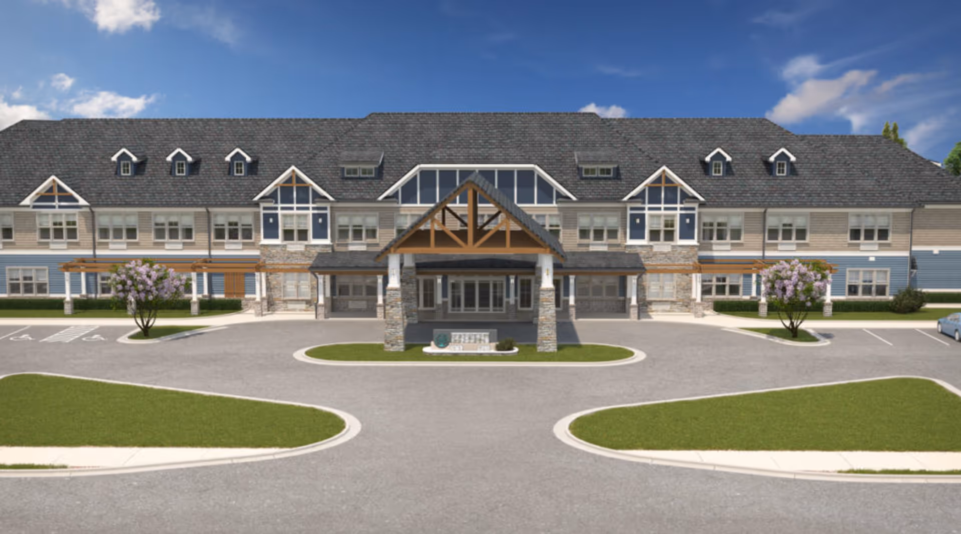 Front exterior view of a large senior living facility building with a peaked roof, multiple windows, and a covered entrance supported by stone pillars. There are landscaped grassy areas and a circular driveway with parking spaces, including handicapped spots, under a blue sky with some clouds.