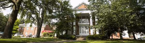 Front entrance of Rathbone Home with brick facade, columns, and surrounding trees.