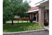 Exterior view of a senior living facility with trees, lawn, and a covered entrance.