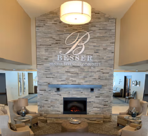 Interior lobby with a stone fireplace, seating area, and a large 'Besser Senior Living Community' sign on the wall.