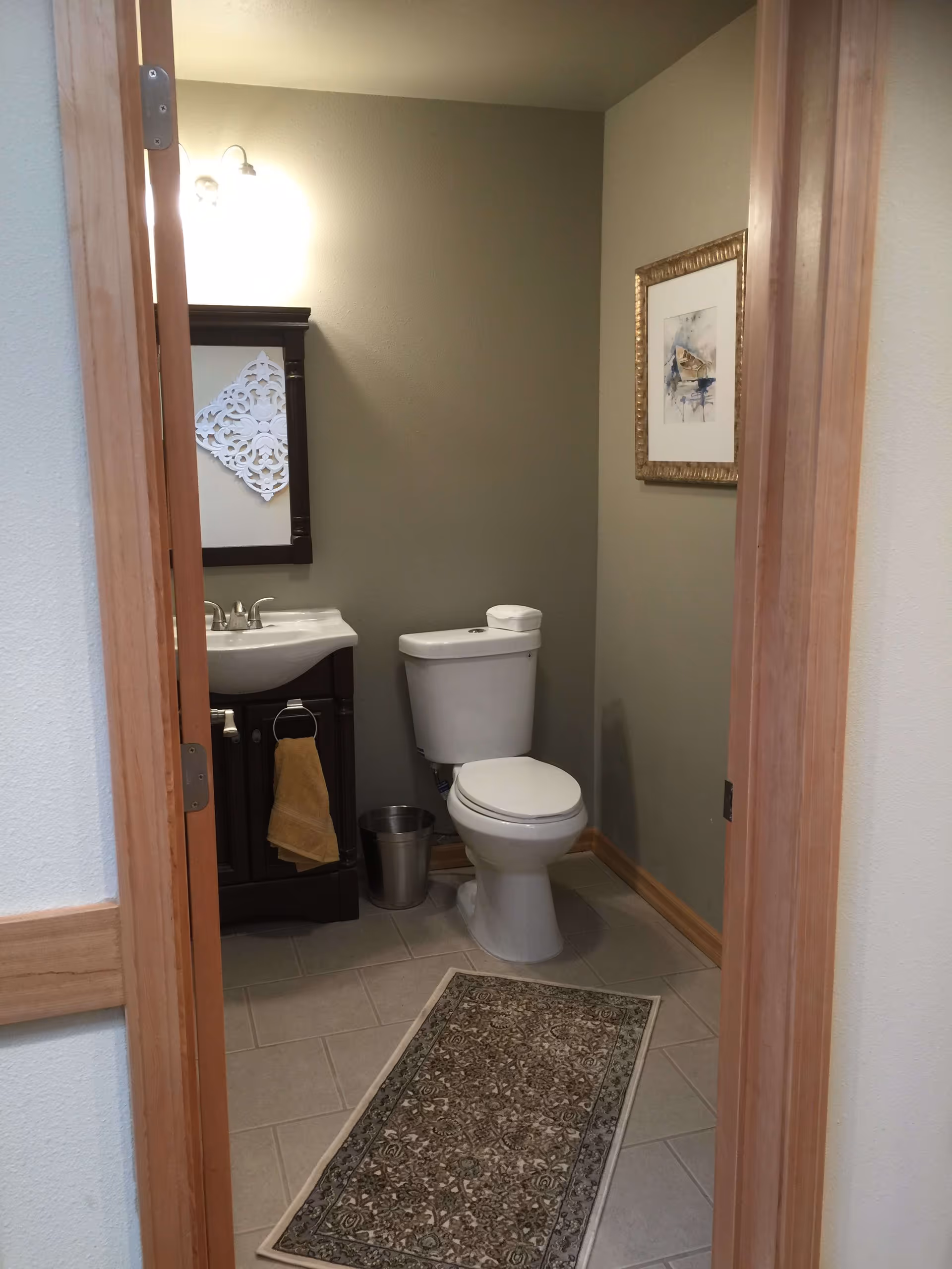 Small bathroom with a toilet, sink vanity and mirror, decorative rug and wall art.