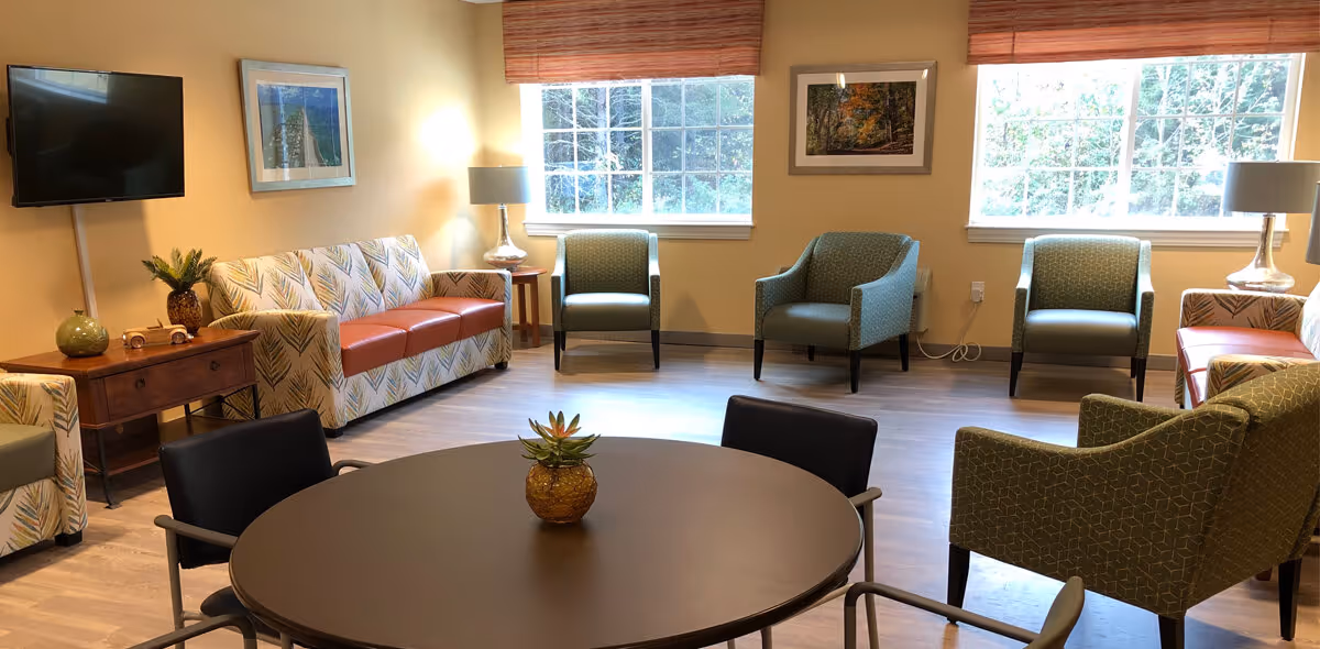 Bright common room with sofas, armchairs, a round table, and large windows.