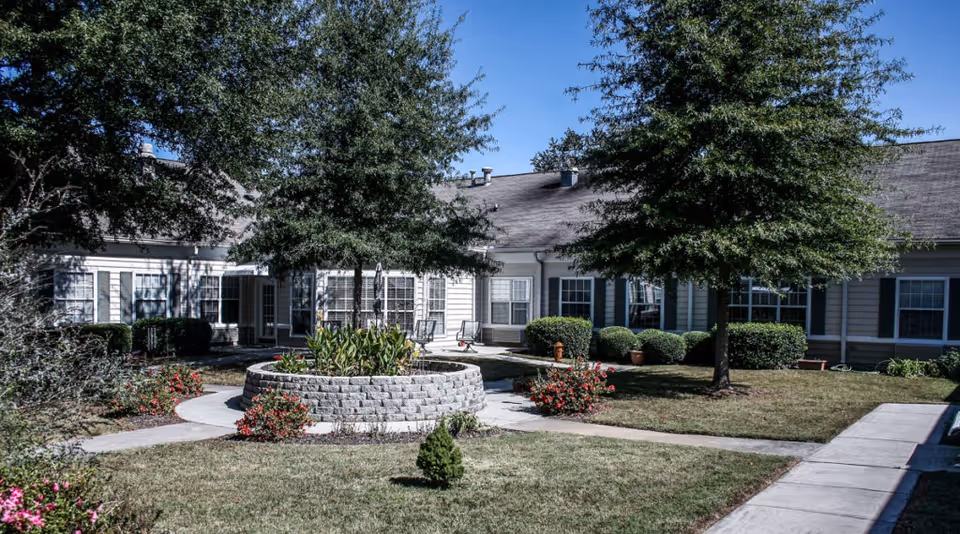Single-story senior living facility with a circular stone planter in a landscaped courtyard.