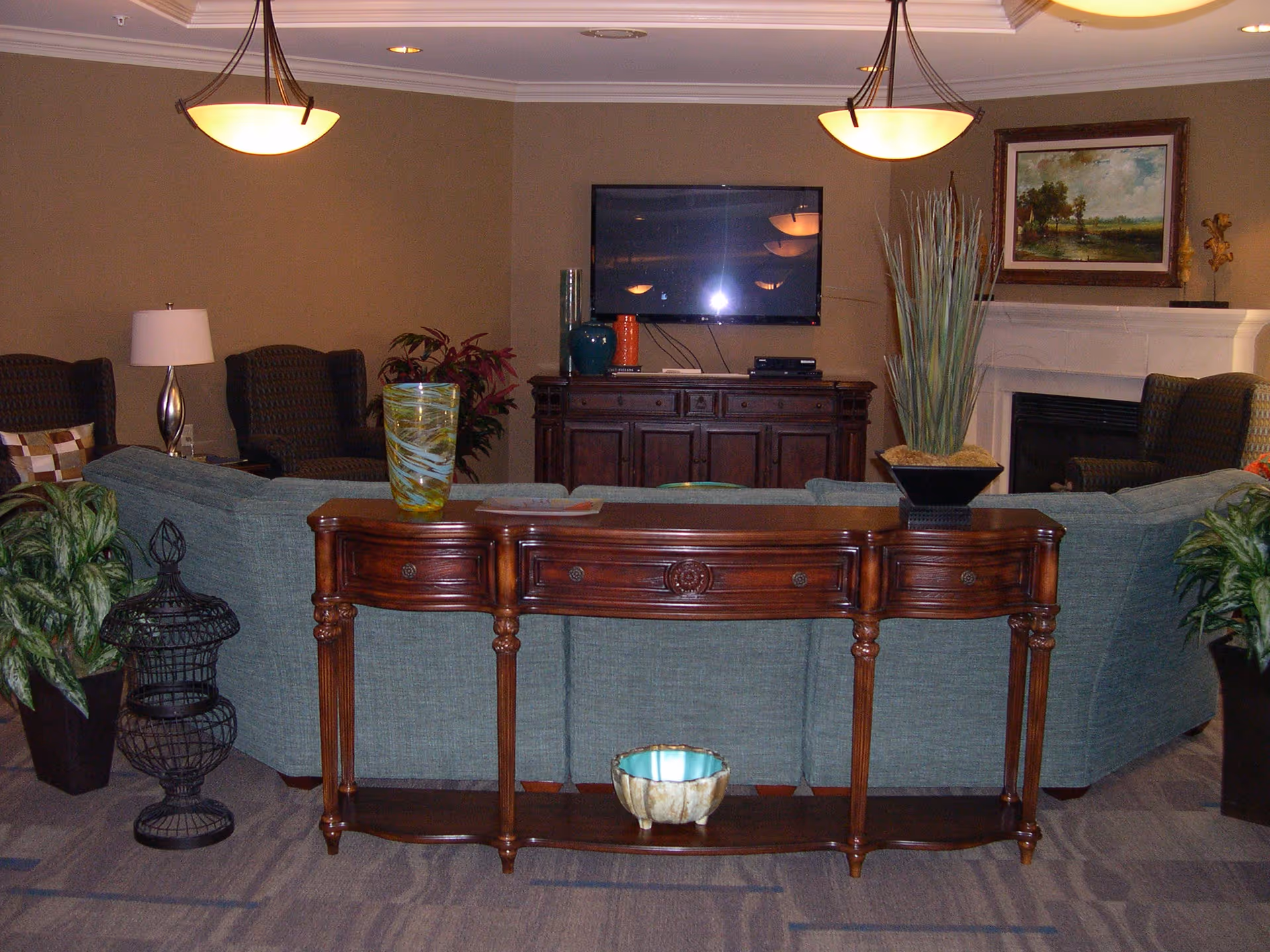 A cozy living room in a senior living facility featuring a green sofa, decorative flowers, and a television.