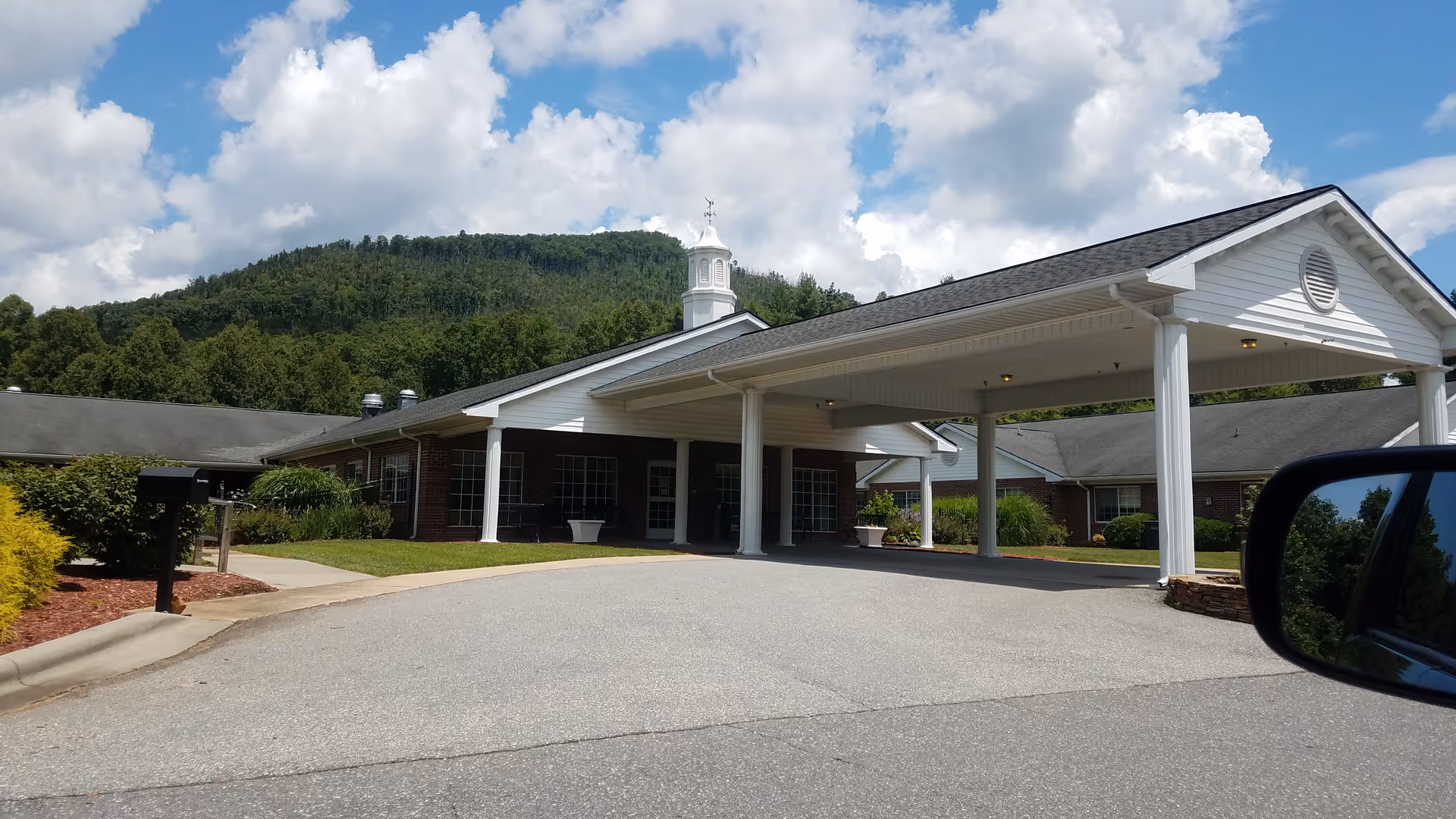 Senior living facility with a covered entrance and mountain backdrop under a bright blue sky.
