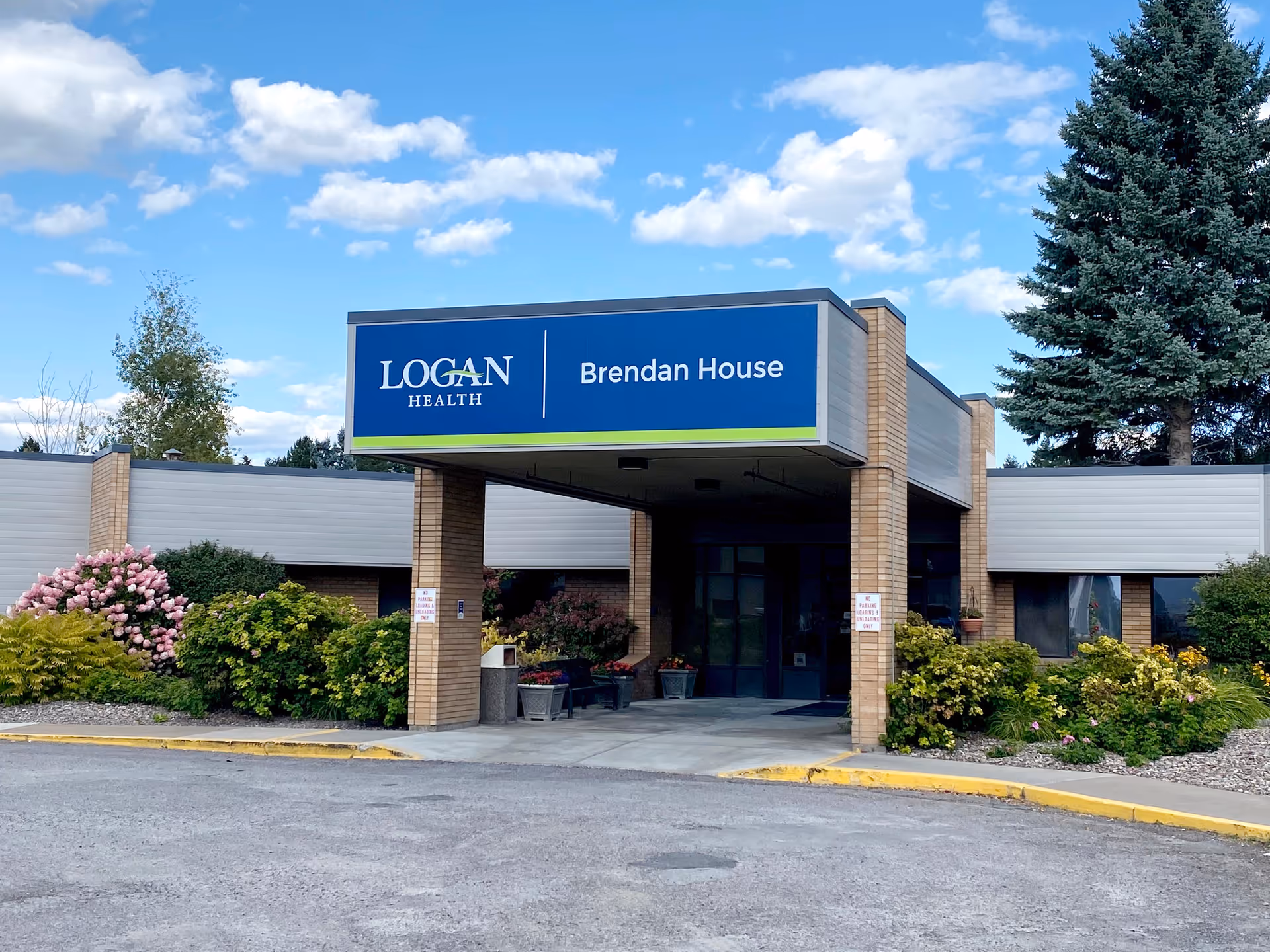 Front entrance of Logan Health Brendan House showing a covered porte-cochere with the facility sign and surrounding landscaping.