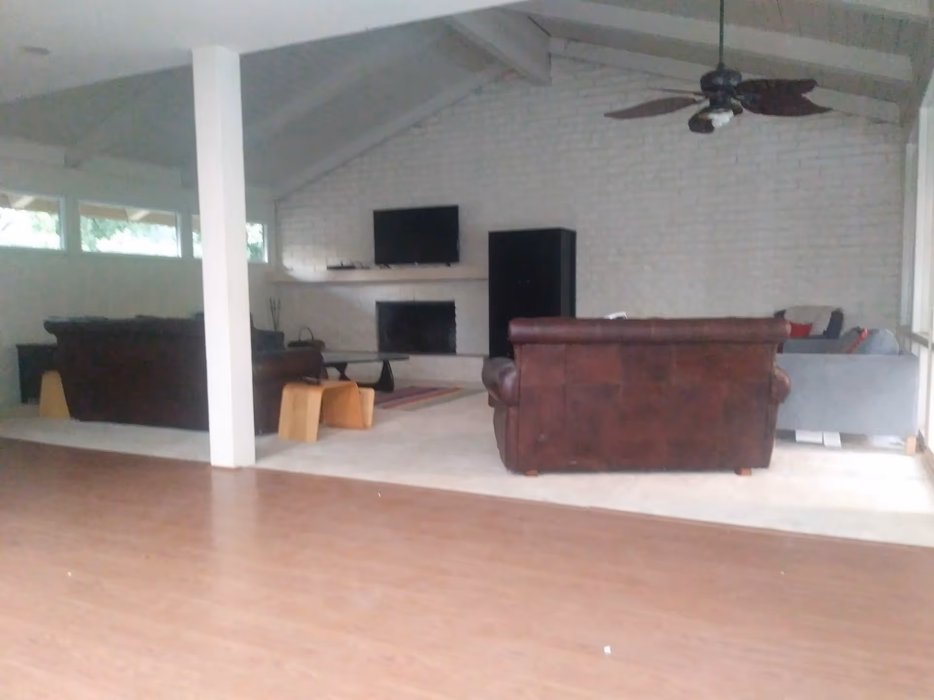 Spacious living room with leather sofas facing a fireplace and wall-mounted TV under a vaulted ceiling with a ceiling fan.
