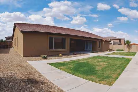 A single-story tan building with a red roof, front lawn, and concrete walkway.