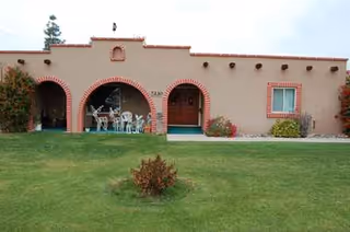 A single-story adobe-style building with arches, lawn, and outdoor seating.