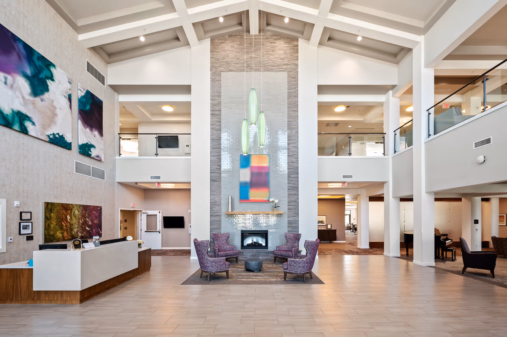 Bright, spacious two-story assisted living lobby with a central fireplace, seating area, reception desk, and modern artwork.