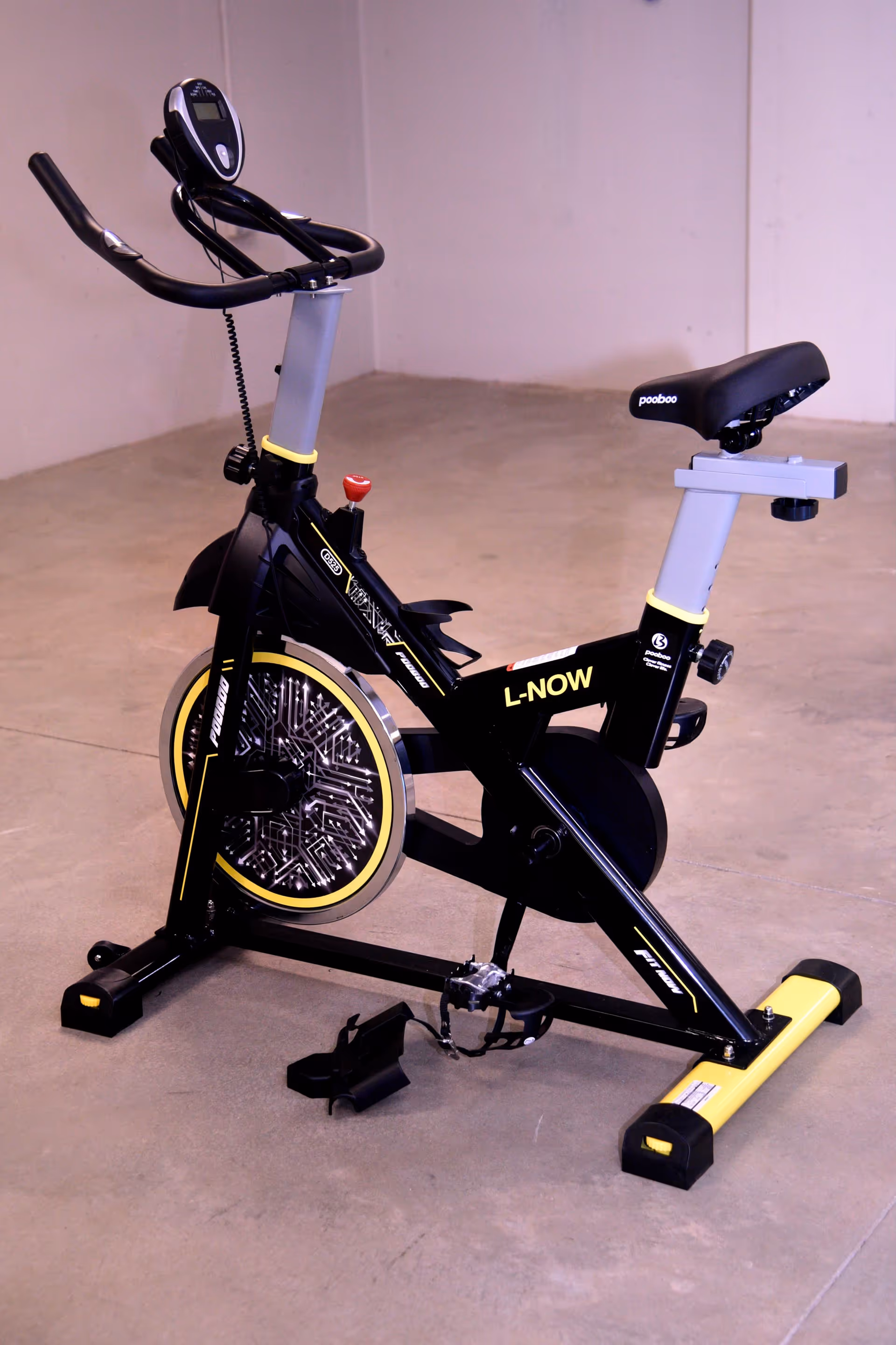A black and yellow stationary exercise bike on a concrete floor against a plain wall.