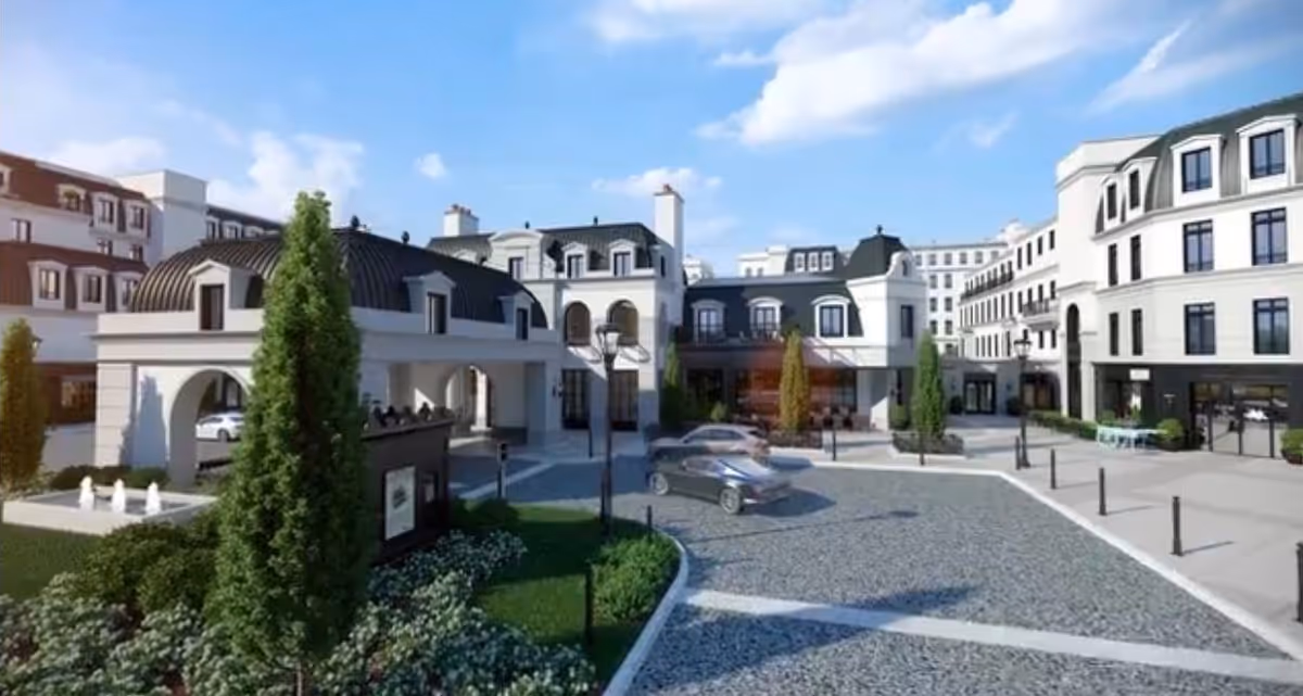 Courtyard and entrance of a grand multi-story senior living building with landscaping, a small fountain, and parked cars under a blue sky.