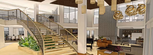 Spacious and modern interior of a senior living facility featuring a wide wooden staircase with metal railings, large windows allowing natural light, multiple seating areas with sofas and chairs, decorative hanging lights, and a fireplace in the background.