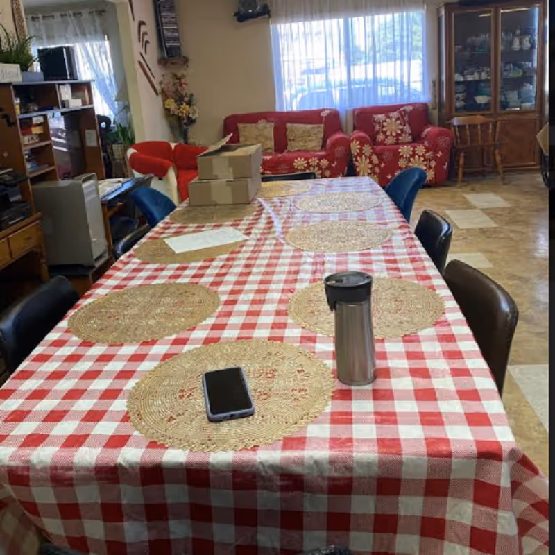Interior common area with a long checkered dining table, chairs, and red floral couches.
