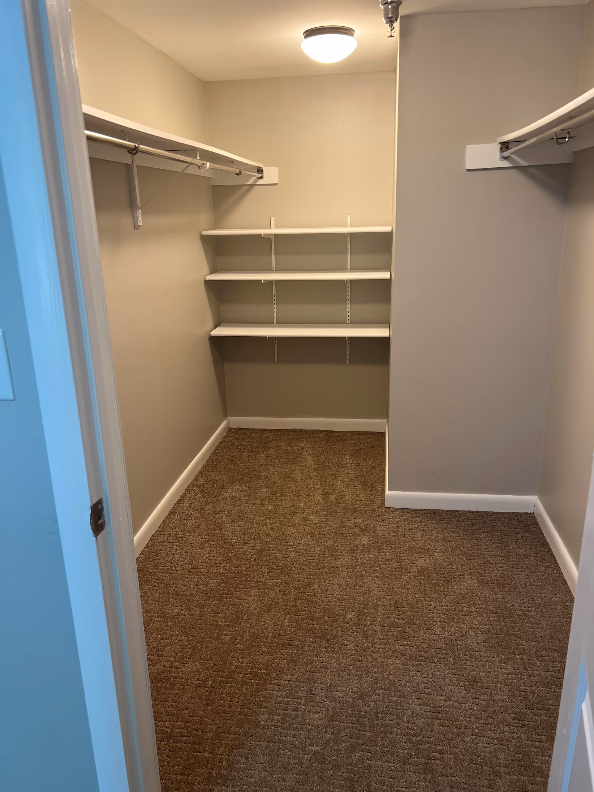 Narrow walk-in closet with shelves and hanging rods in neutral tones.