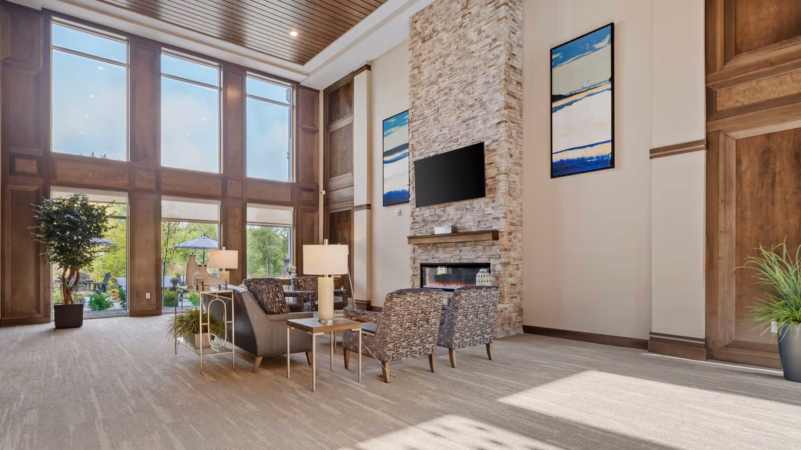 Spacious two-story lounge with large windows, a seating area around a stone fireplace and wall-mounted TV.
