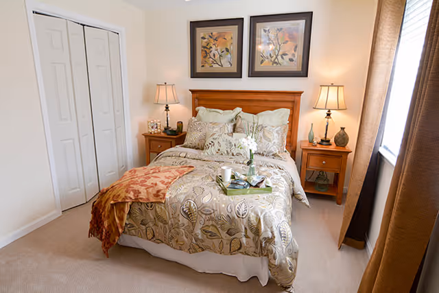 Well-lit bedroom with a made double bed, wooden headboard, two nightstands with lamps, and framed artwork above the bed.