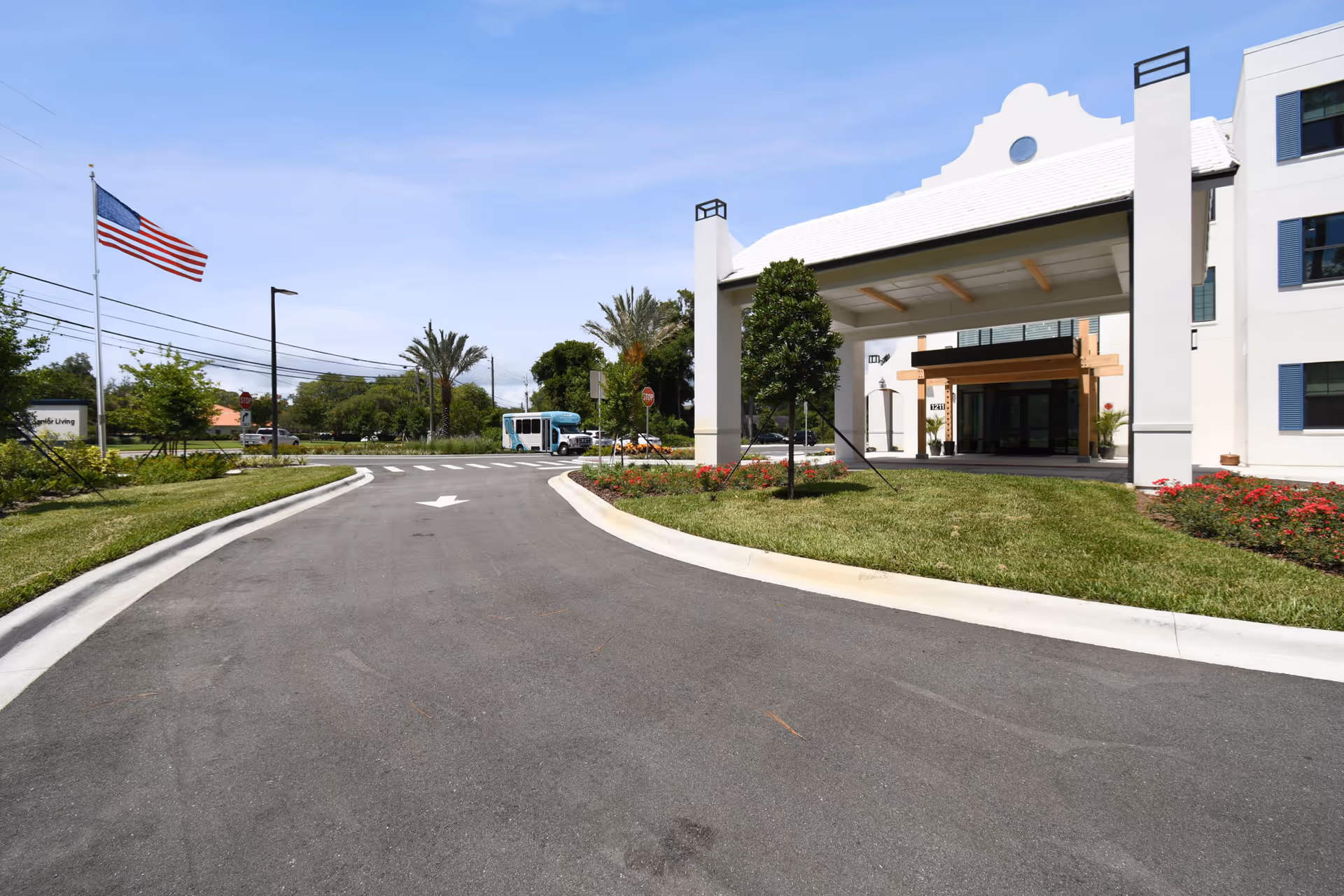 Driveway leading to the covered entrance and porte-cochere of a senior living facility with landscaped islands and an American flag.