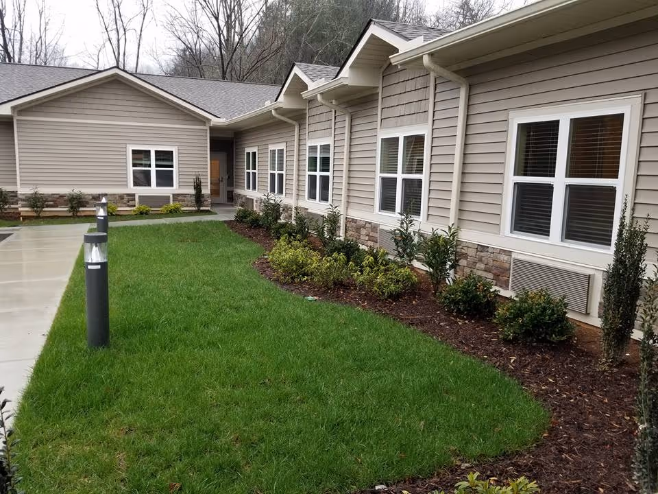 Front exterior of a single-story senior living building with a manicured lawn, walkway, and landscaped bushes.