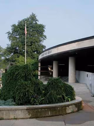 Exterior view of Baldwin House entrance with curved canopy, concrete pillars, and surrounding greenery.
