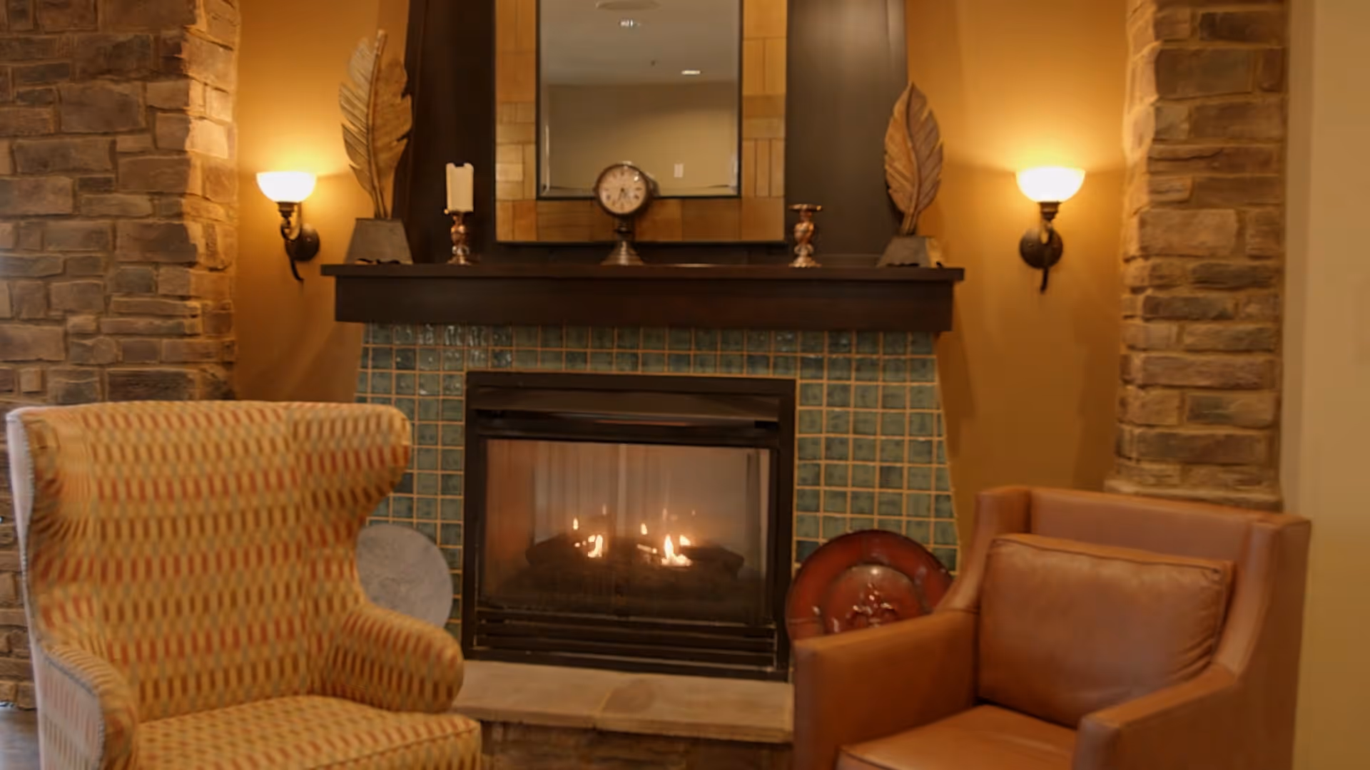 Cozy seating area with two armchairs facing a lit fireplace set in a tiled surround and stone columns.