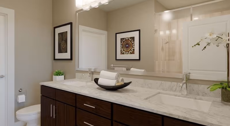 Spacious bathroom featuring a marble countertop vanity with undermount sink, dark wood cabinets, large mirror, toilet and framed artwork.