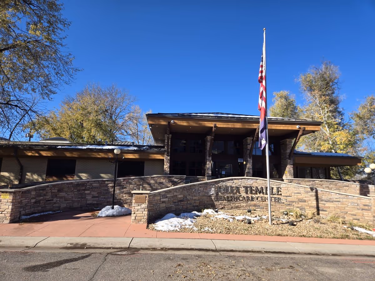 Front exterior of Julia Temple Healthcare Center featuring a stone entrance wall, flagpole, and clear blue sky.