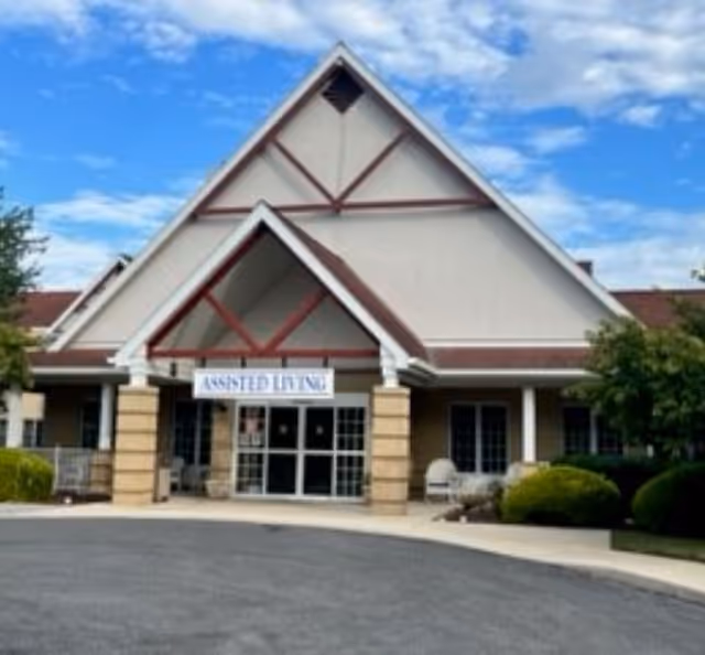 Front exterior of an assisted living facility showing the main entrance under a large peaked roof and a circular driveway.