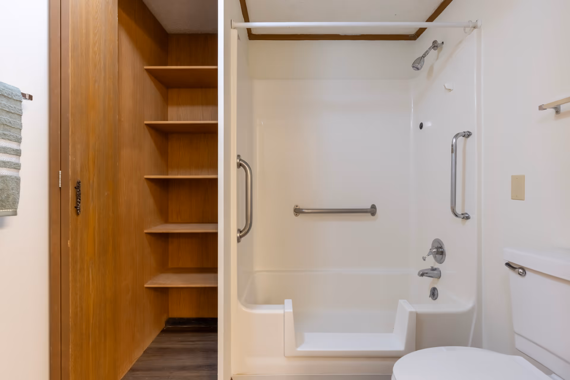 Bathroom showing a walk-in bathtub with grab bars and shower fixtures, a toilet, and adjacent wooden shelving.