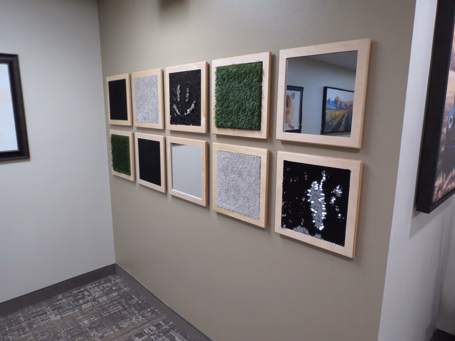 A hallway wall decorated with a 3x4 grid of framed textured panels and mirrors.