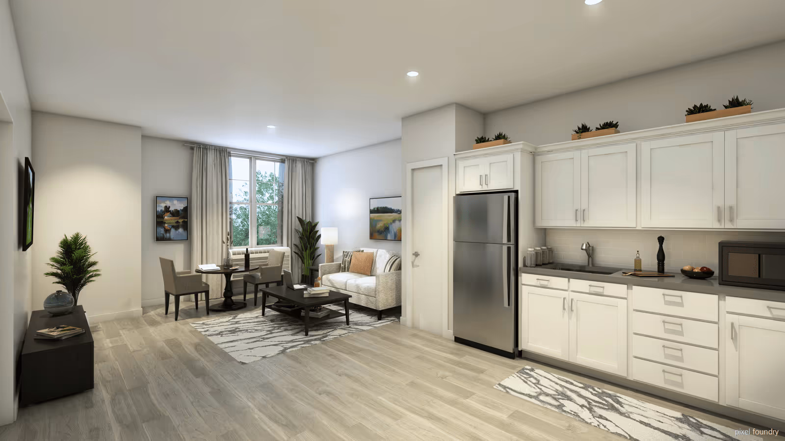 A modern open-concept living space featuring a kitchen with white cabinets, a stainless steel refrigerator, a microwave, and a sink. Adjacent to the kitchen is a living room area with a beige sofa, a coffee table, a floor lamp, and a small dining table with two chairs near a window with curtains. The room has light wood flooring and neutral-colored walls with framed artwork and potted plants for decoration.