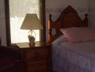 A cozy bedroom with a wooden headboard, quilted bed, nightstand, lamp, and window.