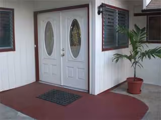 Entrance to a senior living facility with double doors, oval glass panes, and a potted plant.