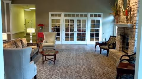Communal living room with upholstered chairs and sofas, a coffee table, fireplace, and French doors.