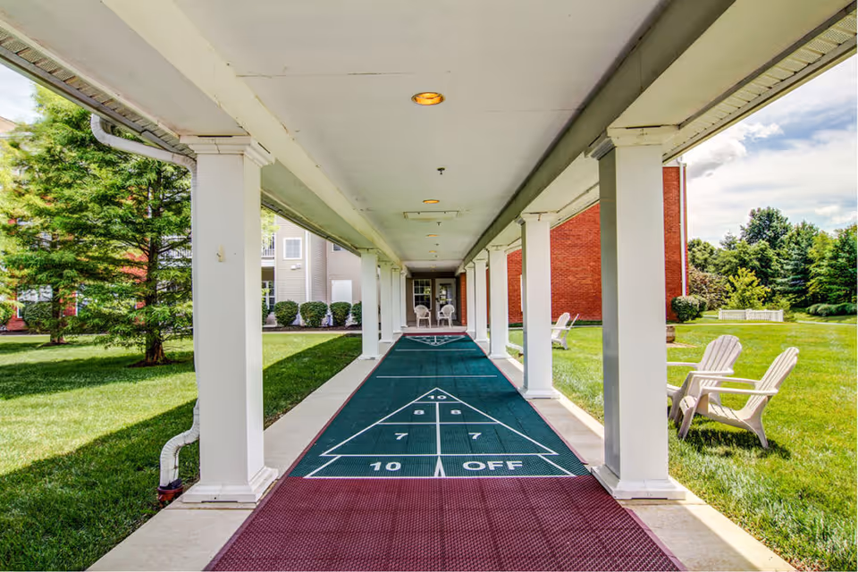 Covered outdoor shuffleboard court running down a columned walkway with grass and Adirondack chairs on either side.