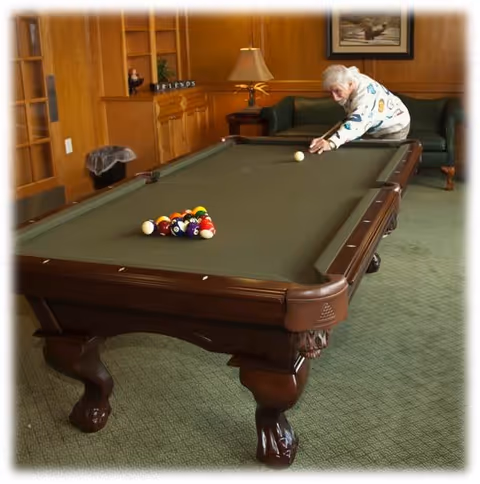 An elderly man leans over a pool table in a wood-paneled common room preparing to take a shot.