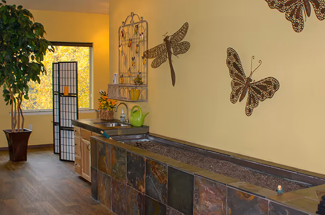 Indoor common area with a long tiled planter and sink, butterfly wall art, a potted tree, and a folding screen by a window.